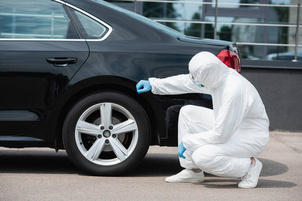 Border guard in hazmat suit and latex gloves checking car outdoors  - Foto, afbeelding