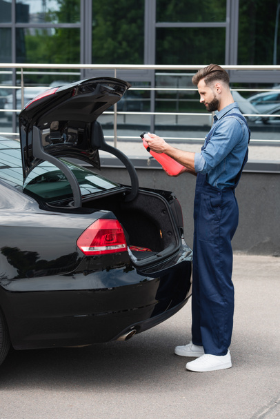 Side view of mechanic looking at canister of windshield washer fluid near car  - Foto, Bild