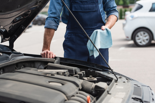 Cropped view of mechanic holding rag near auto with open hood outdoors  - Fotografie, Obrázek