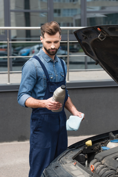 Mechanic holding bottle of polish and rag near car outdoors  - 写真・画像