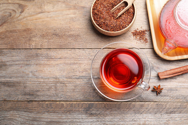 Freshly brewed rooibos tea, scattered dry leaves and spices on wooden table, flat lay. Space for text - Foto, Bild