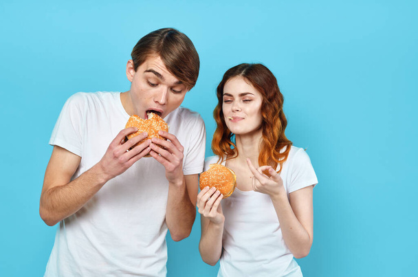 jovem casal em camisetas brancas com hambúrgueres em suas mãos fast food lanche - Foto, Imagem