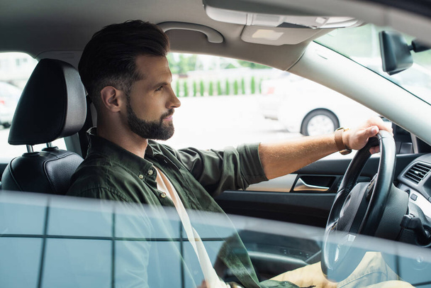 Side view of young bearded man driving car outdoors  - Photo, Image