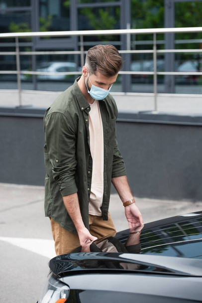 Ο άνθρωπος με την ιατρική μάσκα άνοιγμα κουκούλα του αυτοκινήτου  - Φωτογραφία, εικόνα