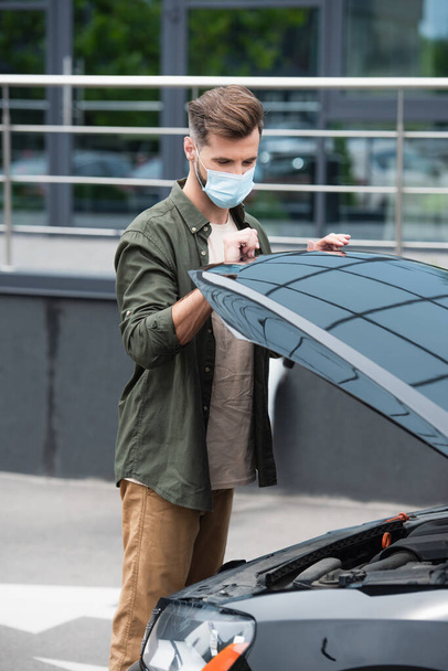Řidič v lékařské masce otvírání kapoty auta venku  - Fotografie, Obrázek