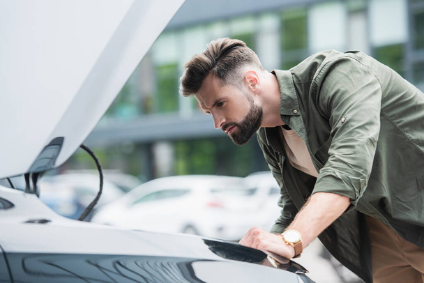 Side view of focused man looking at car with open hood  - Photo, Image