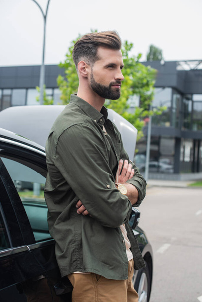 Side view of young man standing with crossed arms near car outdoors  - Фото, зображення