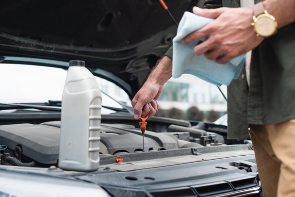 Cropped view of man checking oil of engine near bottle on car  - Photo, Image