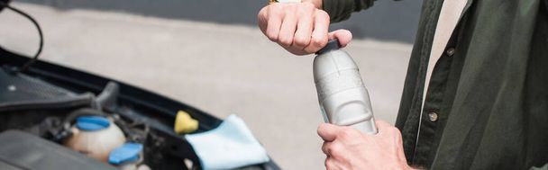 Cropped view of man opening bottle of engine oil near car, banner  - Foto, imagen
