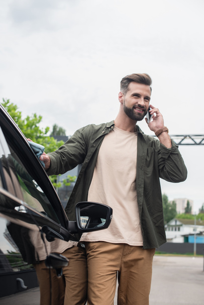 Smiling driver talking on mobile phone while cleaning car outdoors  - Foto, immagini
