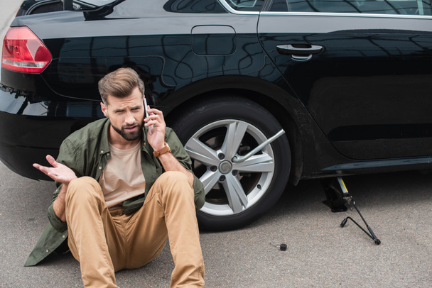 Mężczyzna mówi na smartfonie w pobliżu samochodu z kluczykiem i podnieś jack  - Zdjęcie, obraz