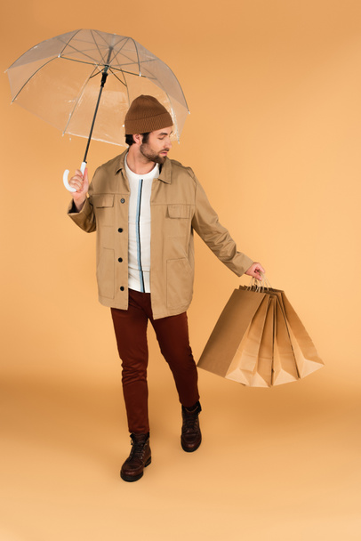 man in brown pants and jacket carrying shopping bags under umbrella on beige - Valokuva, kuva