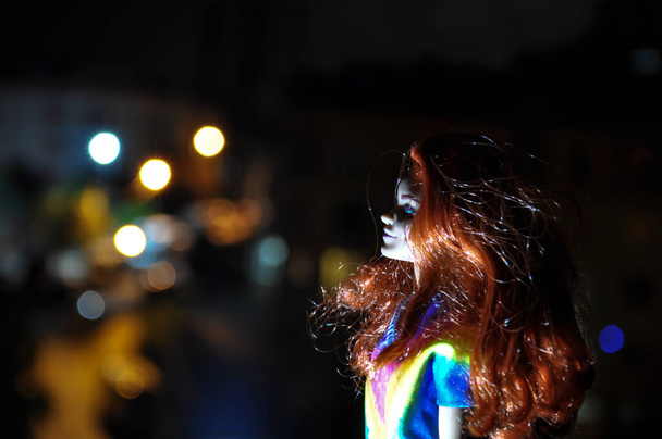 Silhouette eines weiblichen Gesichts auf hellem Hintergrund. SIlhouette einer einsamen Puppe mit langen Haaren bei Nacht mit Stadtbeleuchtung im Hintergrund. Selektiver Fokus - Foto, Bild