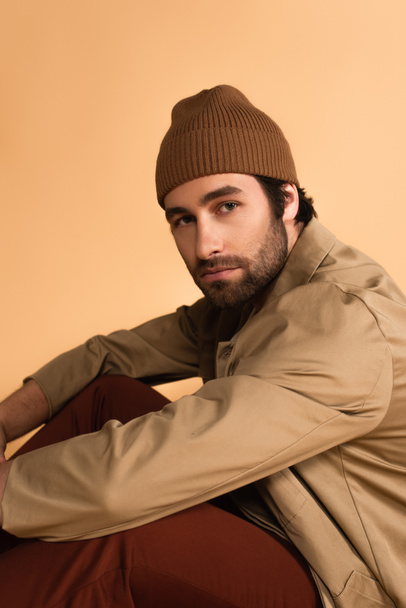 young man in brown beanie and jacket looking at camera isolated on beige - Foto, imagen