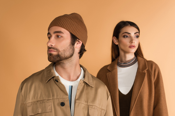 trendy man in beanie looking aside near blurred stylish woman isolated on beige - Foto, Imagem