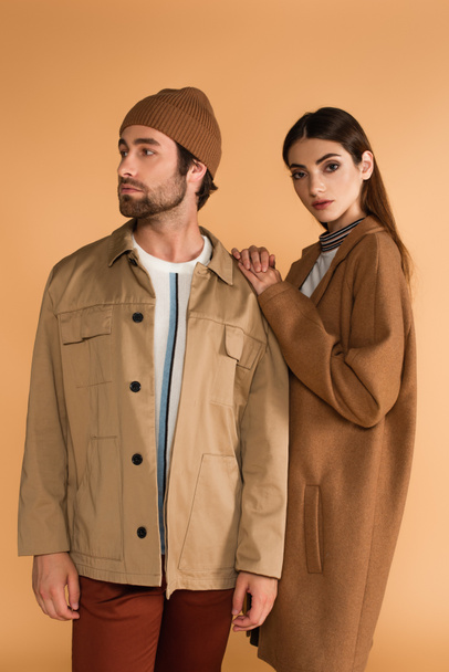 fashionable woman leaning on shoulder of trendy man in beanie isolated on beige - Φωτογραφία, εικόνα