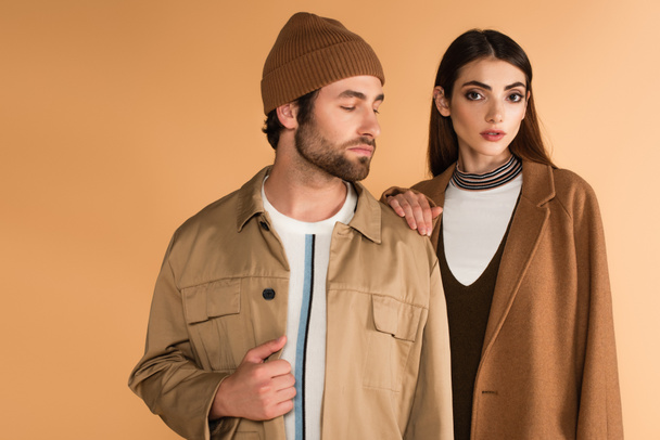 stylish woman touching shoulder of trendy man in beanie isolated on beige - Fotografie, Obrázek