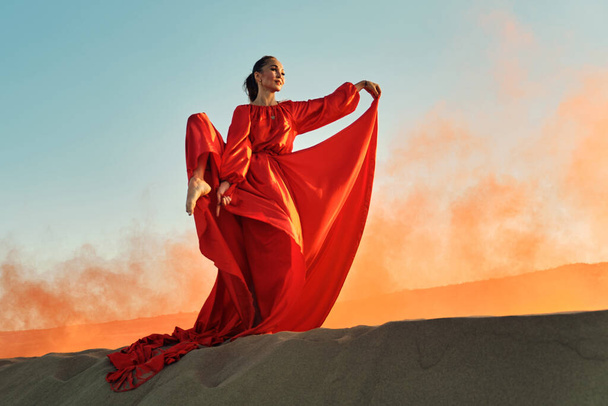 Γυναίκα με κόκκινο φόρεμα χορεύει στην έρημο στον γαλάζιο ουρανό - Φωτογραφία, εικόνα