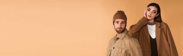 trendy woman leaning on stylish man in brown beanie isolated on beige, banner - Zdjęcie, obraz