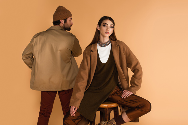 back view of man in jacket near stylish woman sitting on stool isolated on beige - Foto, immagini