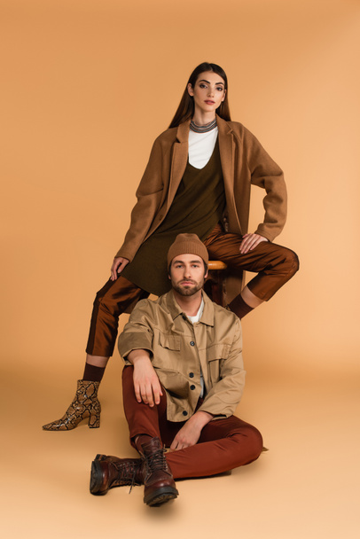 young couple in stylish autumn outfit looking at camera while posing on beige background - Valokuva, kuva