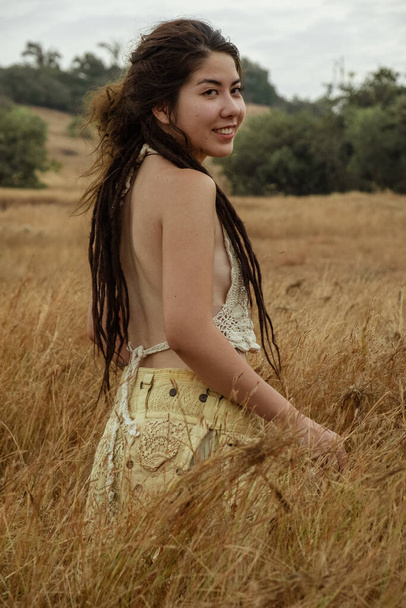Πορτρέτο του χαμογελώντας νεαρή γυναίκα στέκεται σε ξηρό γρασίδι - Φωτογραφία, εικόνα