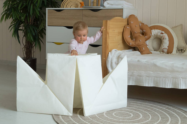 A one-year-old child plays in the children's room with a huge white paper boat in the origami technique - Foto, Imagen
