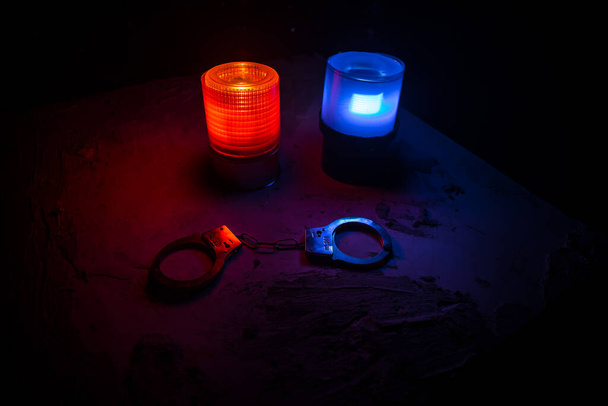 Polizeirazzia in der Nacht und Sie stehen unter Arrest. Silhouette von Handschellen mit blinkenden roten und blauen Polizeilichtern vor nebligem Hintergrund. Selektiver Fokus - Foto, Bild