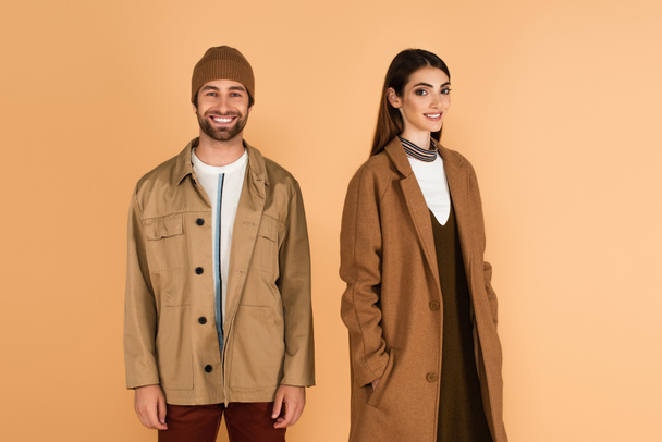 happy couple in trendy autumn clothes looking at camera isolated on beige - Zdjęcie, obraz