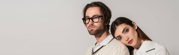young woman leaning on back of man in stylish eyeglasses isolated on grey, banner - Foto, imagen