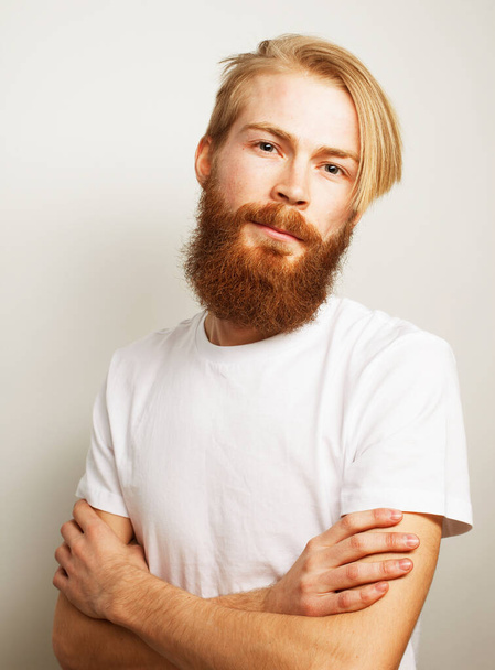 Waist-up shot of young man with red hair wearing white t-shirt looking at camera with crossed arms over white background - Valokuva, kuva