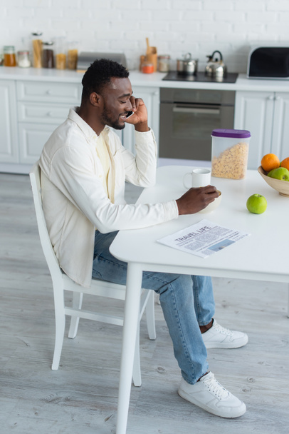 cheerful african american man talking on smartphone while having breakfast  - Фото, изображение