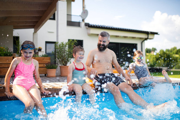 Father with three daughters outdoors in tha backyard, sitting by swimming pool. - Photo, image