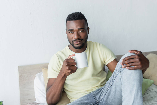 アフリカ系アメリカ人の男性が寝室でコーヒーを飲み - 写真・画像