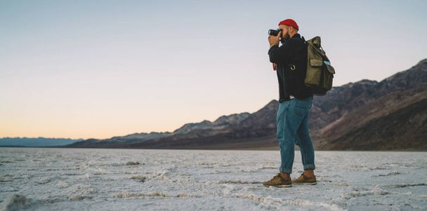 Side view of full body male traveler with photo camera in hands taking picture of amazing landscape in Badwater Basin while spending holidays in USA - Фото, зображення