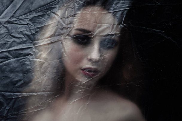Giovane donna triste bellezza intrappolata dietro un foglio di plastica come protezione contro COVID-19. Ben si adatta per la copertina del libro  - Foto, immagini