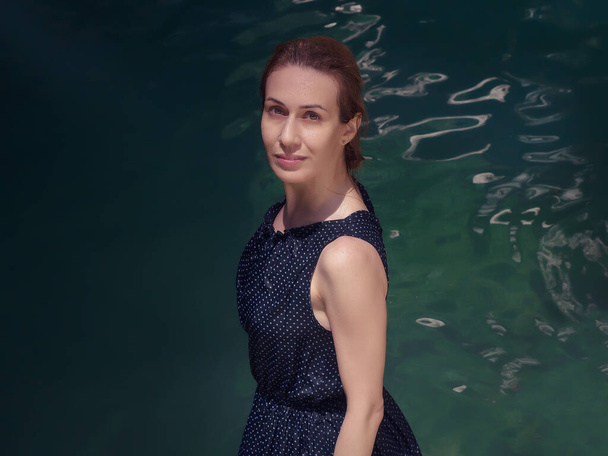 Chica sonriente en vestido mojado se encuentra cerca del agua turquesa bajo los rayos del sol - Foto, Imagen