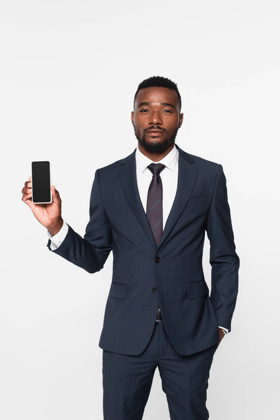 african american businessman in suit holding smartphone with blank screen isolated on grey - Foto, afbeelding