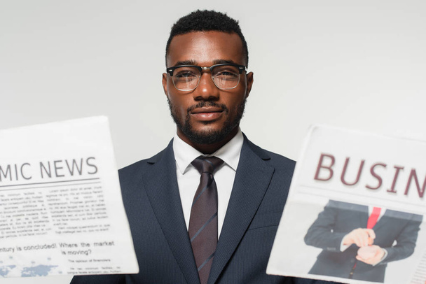 african american man in eyeglasses holding newspapers isolated on grey - Foto, Imagem