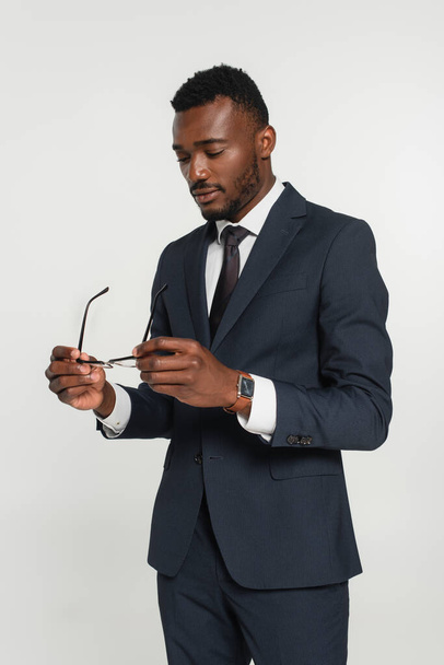 african american man in suit holding eyeglasses isolated on grey - Foto, immagini