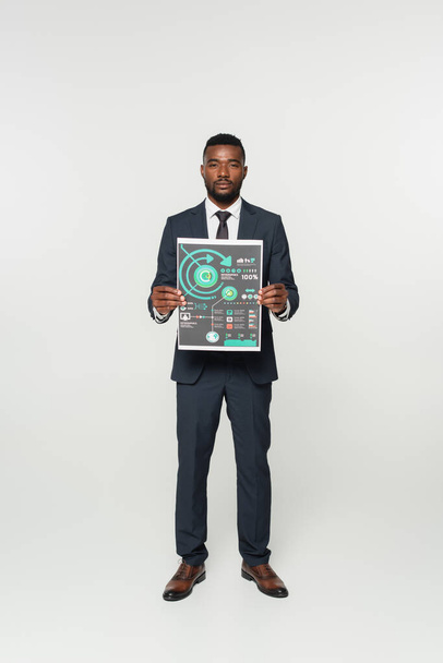 homme d'affaires afro-américain en costume tenant du papier imprimé avec infographies isolées sur gris - Photo, image