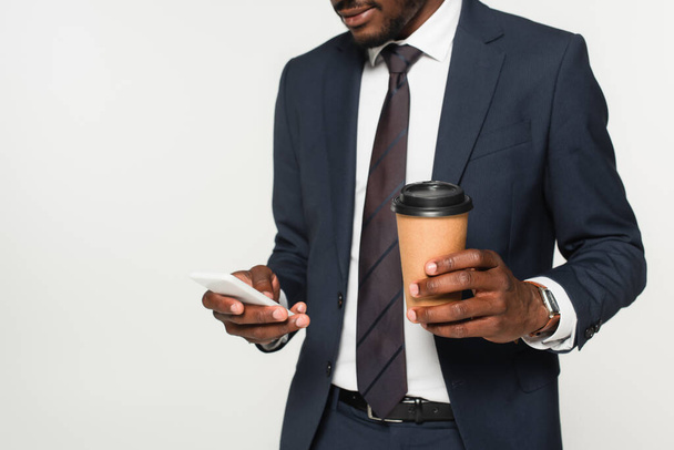 cropped view of african american businessman in suit messaging on smartphone and holding paper cup isolated on grey  - Φωτογραφία, εικόνα