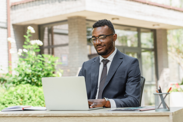 cheerful african american businessman in eyeglasses looking at laptop  - Foto, Imagen