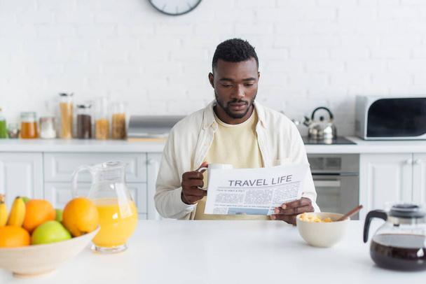 szakállas afro-amerikai férfi kezében csésze kávét és olvasás utazási élet újság  - Fotó, kép