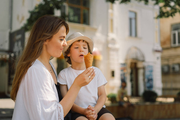  Young mother with small boy outdoors in summer, eating ice cream. Summer food and summer time. - Zdjęcie, obraz