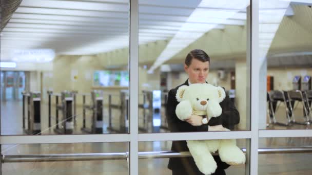 Guy está esperando na plataforma com um urso de brinquedo em suas mãos. - Filmagem, Vídeo