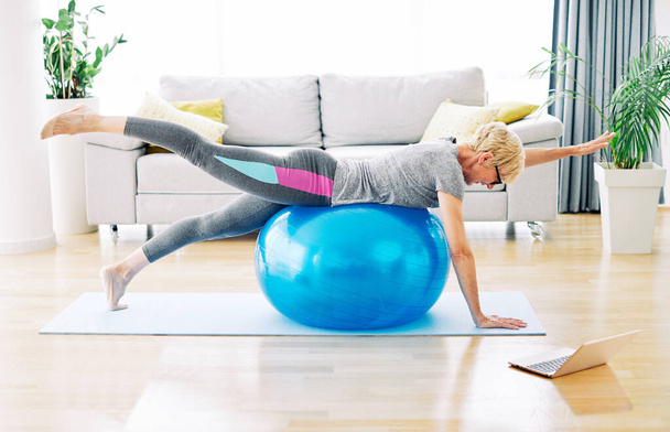 İç mekan egzersiz yapan kadın yaşam stili spor antrenmanı evde sağlıklı spor salonu uygun laptop topu egzersizi yapıyor. - Fotoğraf, Görsel