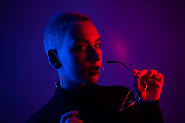 Portrait of beautiful young woman with short hair wearing glasses in neon light - Zdjęcie, obraz