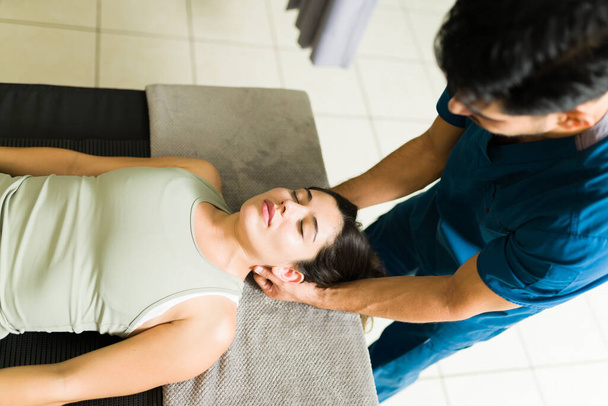 Высокий угол для красивой молодой женщины, получающей массаж шеи и головы от профессиональной латинской физиотерапии - Фото, изображение