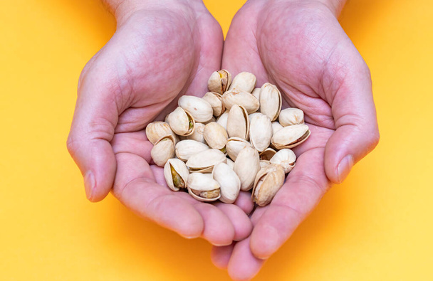 Hands of a person with a handful of pistachios on orange background. nuts. concept care of food and healthy lifestyle - Photo, Image